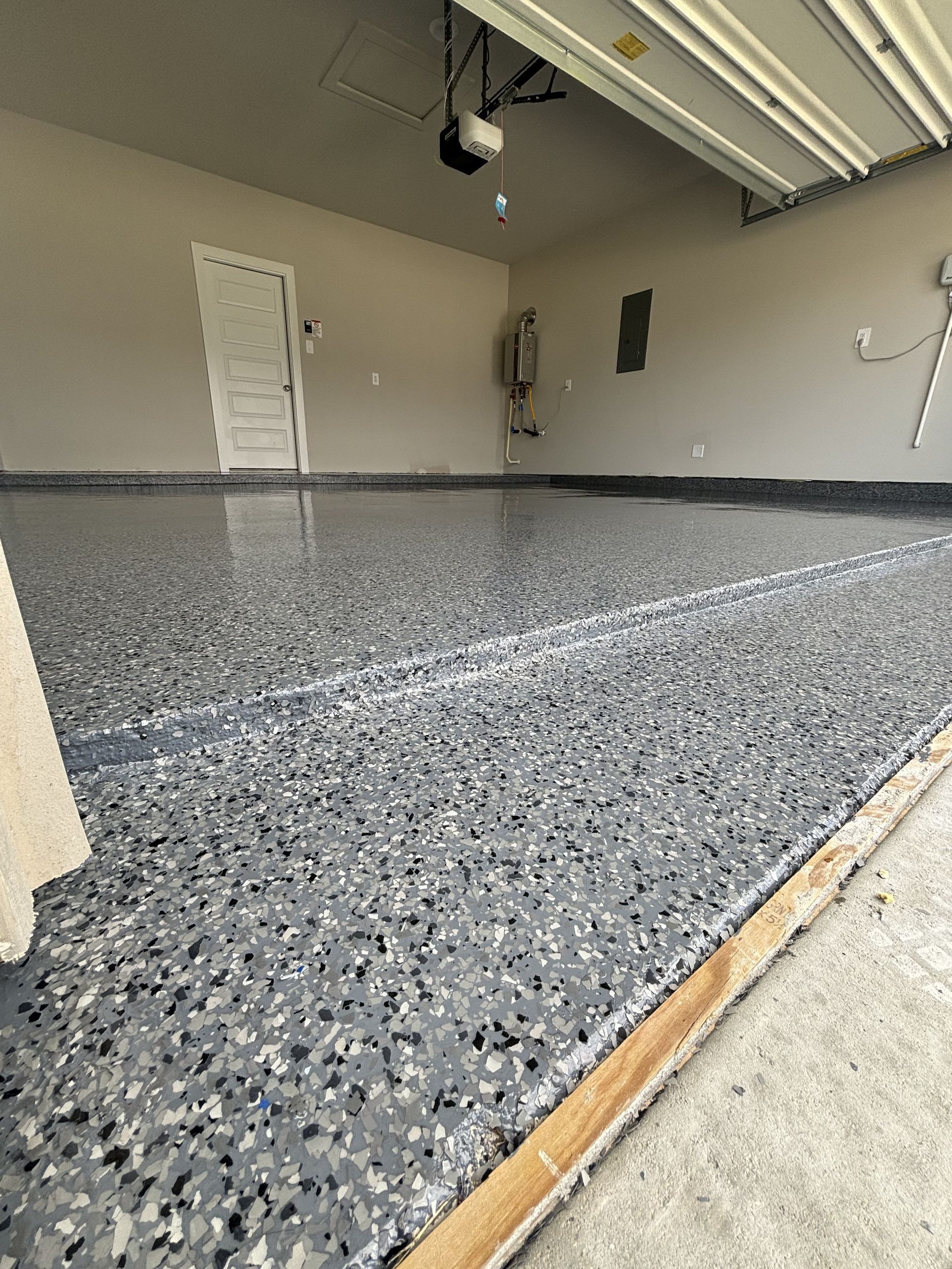 Garage with speckled, gray epoxy floor and closed white door.