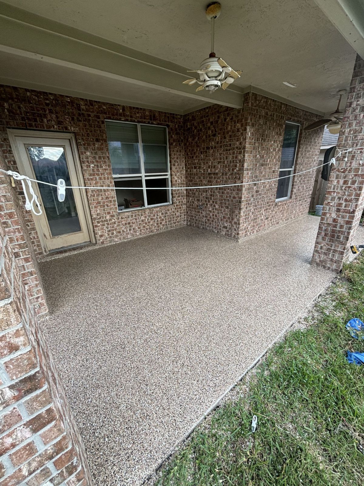 Covered patio with speckled concrete floor and brick walls; a door, windows, and grass are visible.