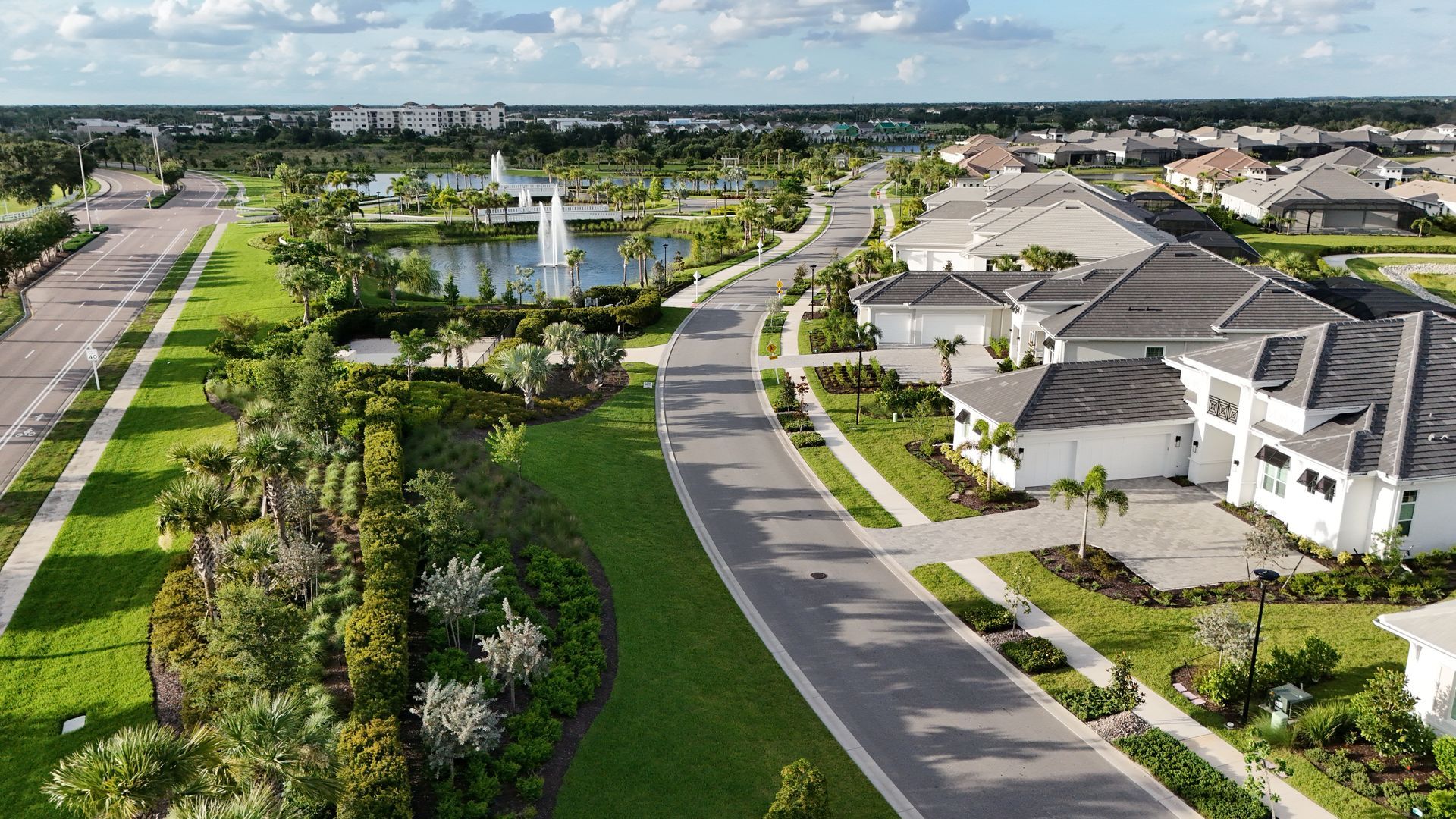 Aerial view of a suburban neighborhood with houses, a road, green lawns, and a pond with a fountain. Aerial view of a suburban neighborhood with houses, a road, green lawns, and a pond with a fountain.