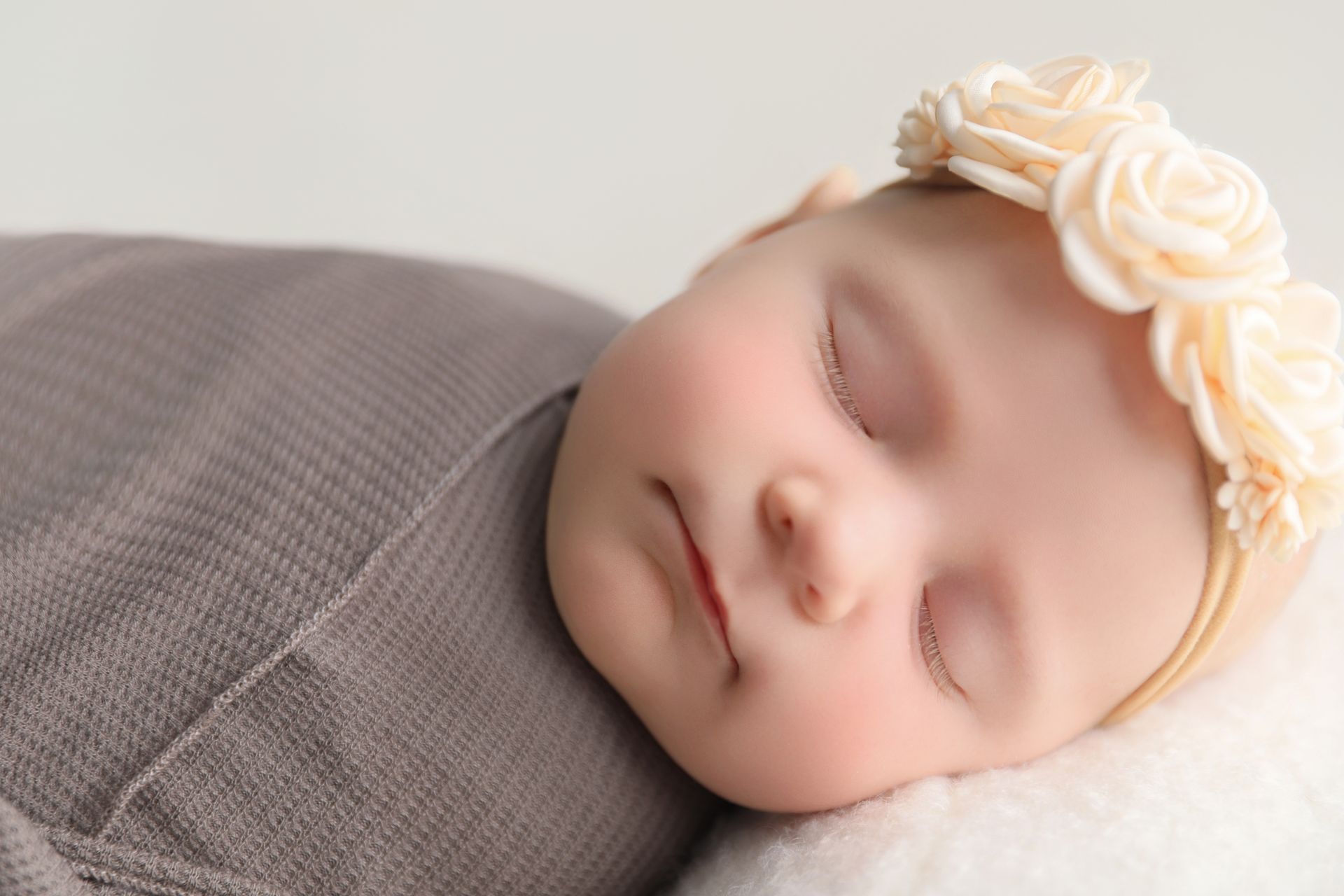 Sleeping baby wrapped in a gray blanket, wearing a floral headband.