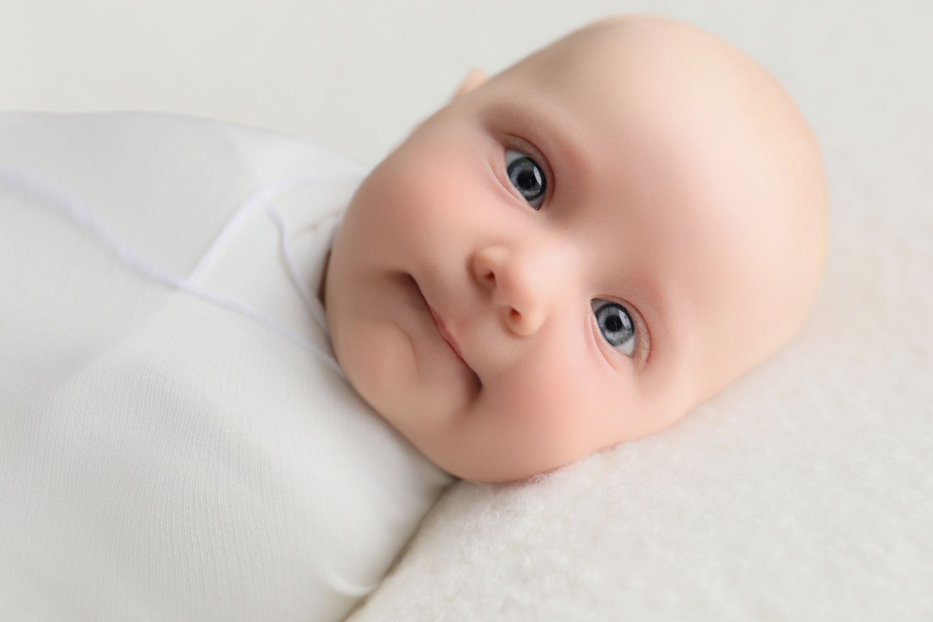Baby with blue eyes, looking at the camera, resting on white fabric.