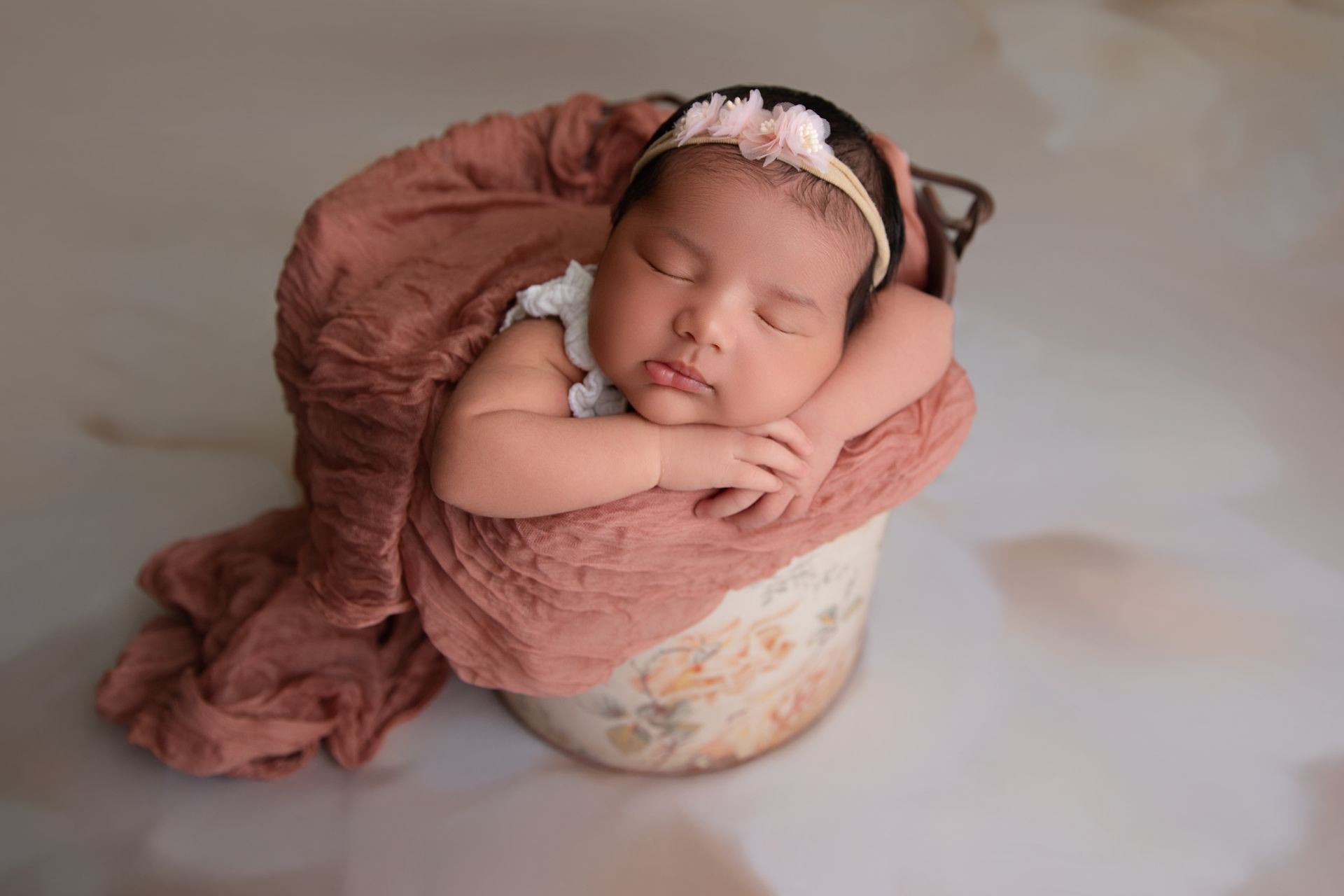 Newborn baby sleeping in a floral bucket, wrapped in a pink blanket.