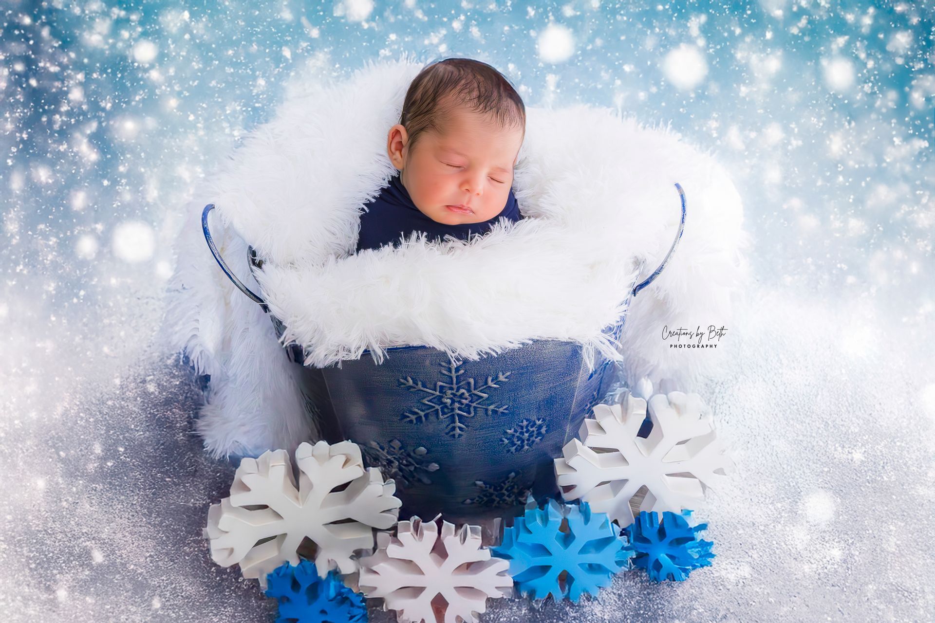 Studio newborn portrait of a baby wrapped in blue with a winter snowflake theme