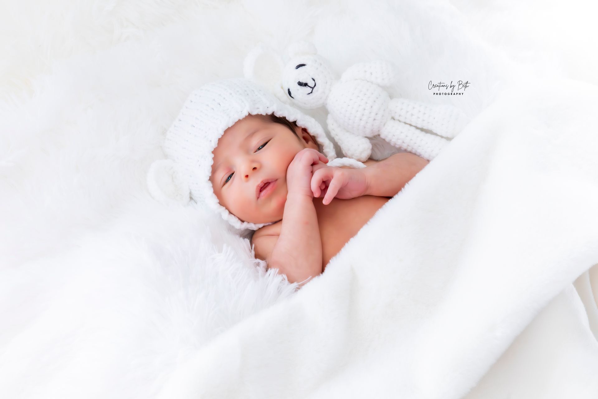 Newborn baby resting on a white blanket with a white teddy bear