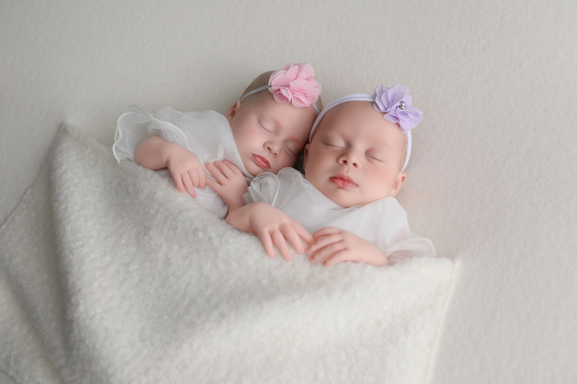 Twin newborn babies wrapped together in a soft neutral setup.