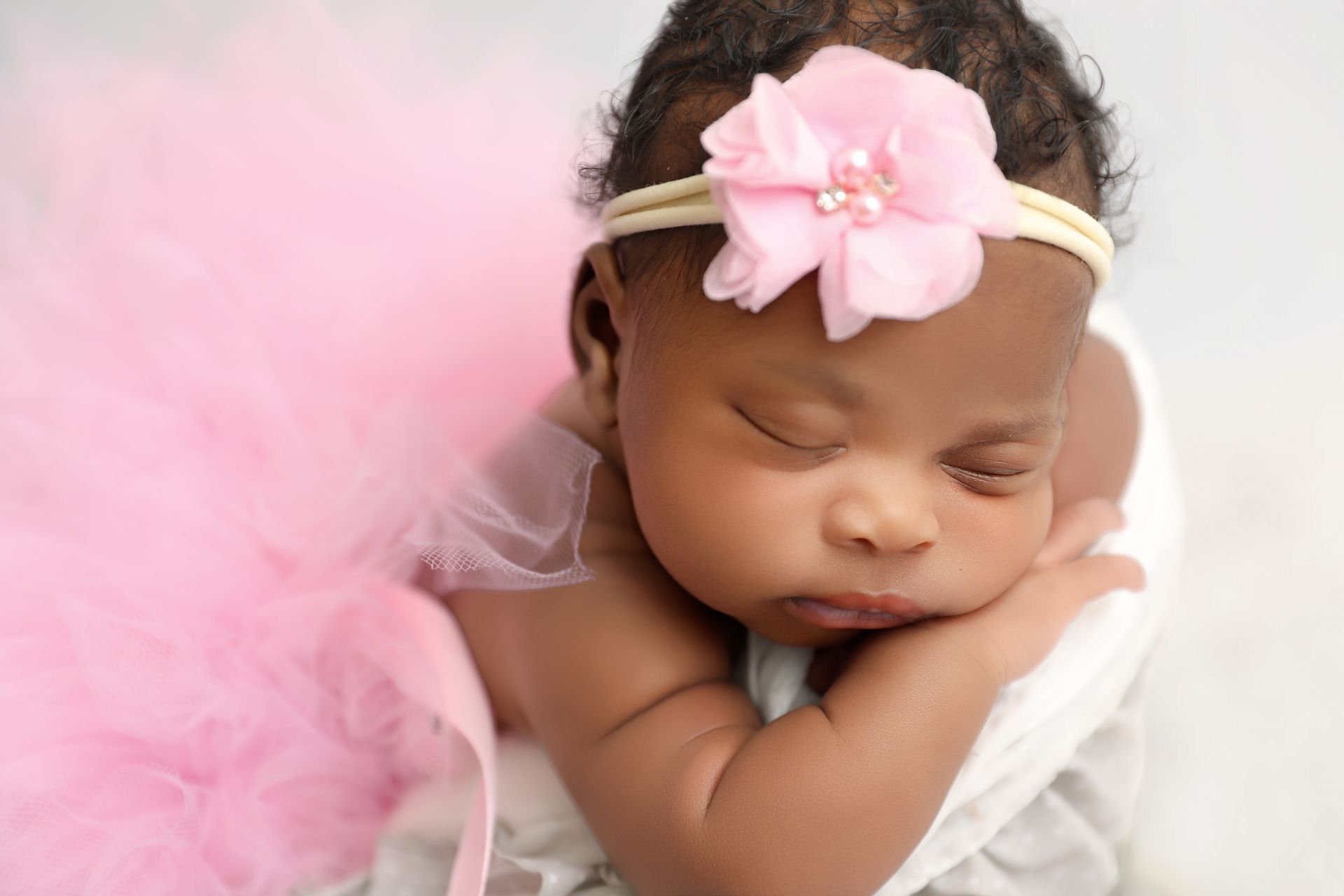Newborn baby sleeping, wearing a pink tutu and headband with a flower.