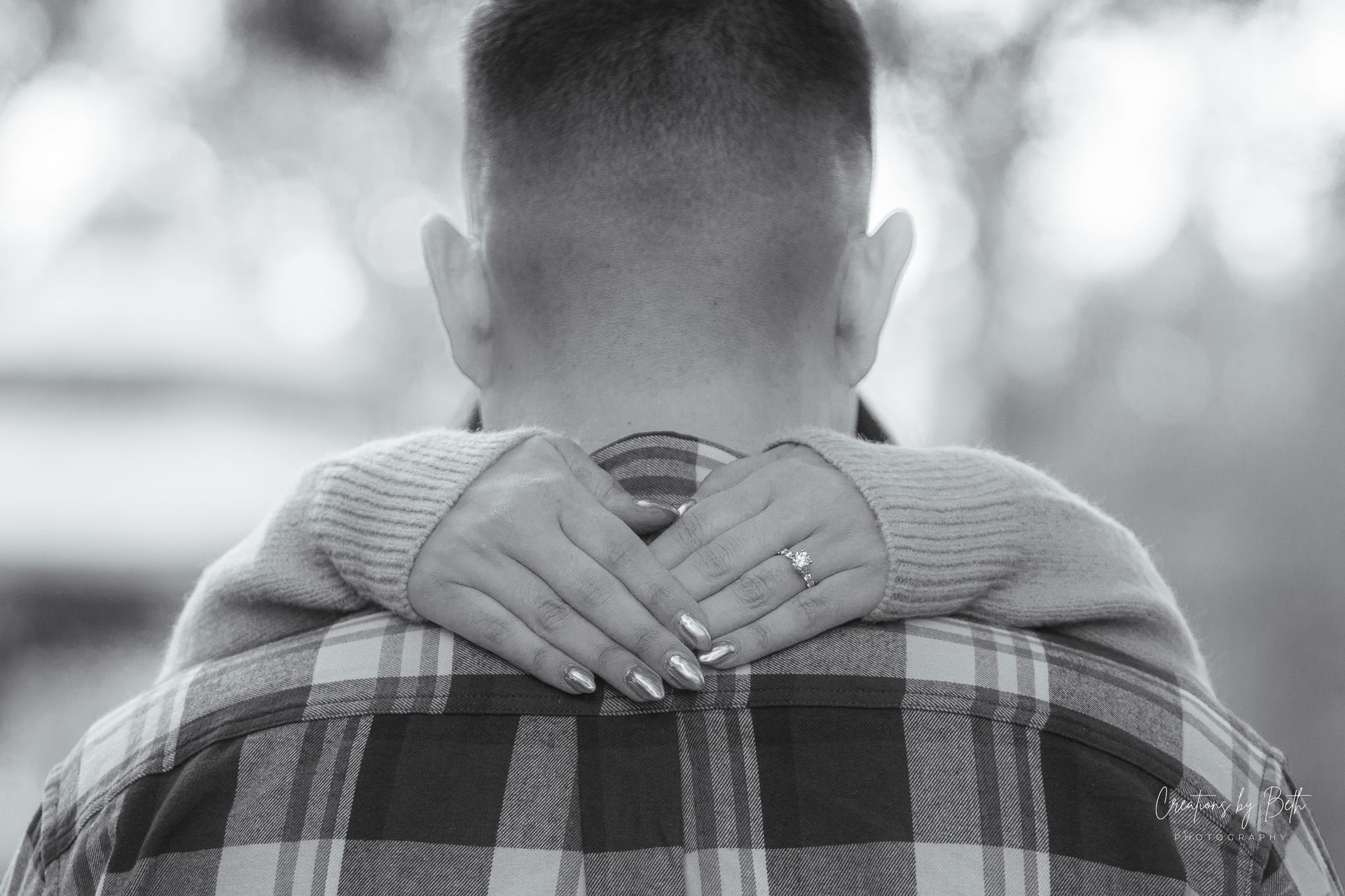 Couple embracing; hands clasped, showing engagement ring. Man in plaid shirt. Black and white.