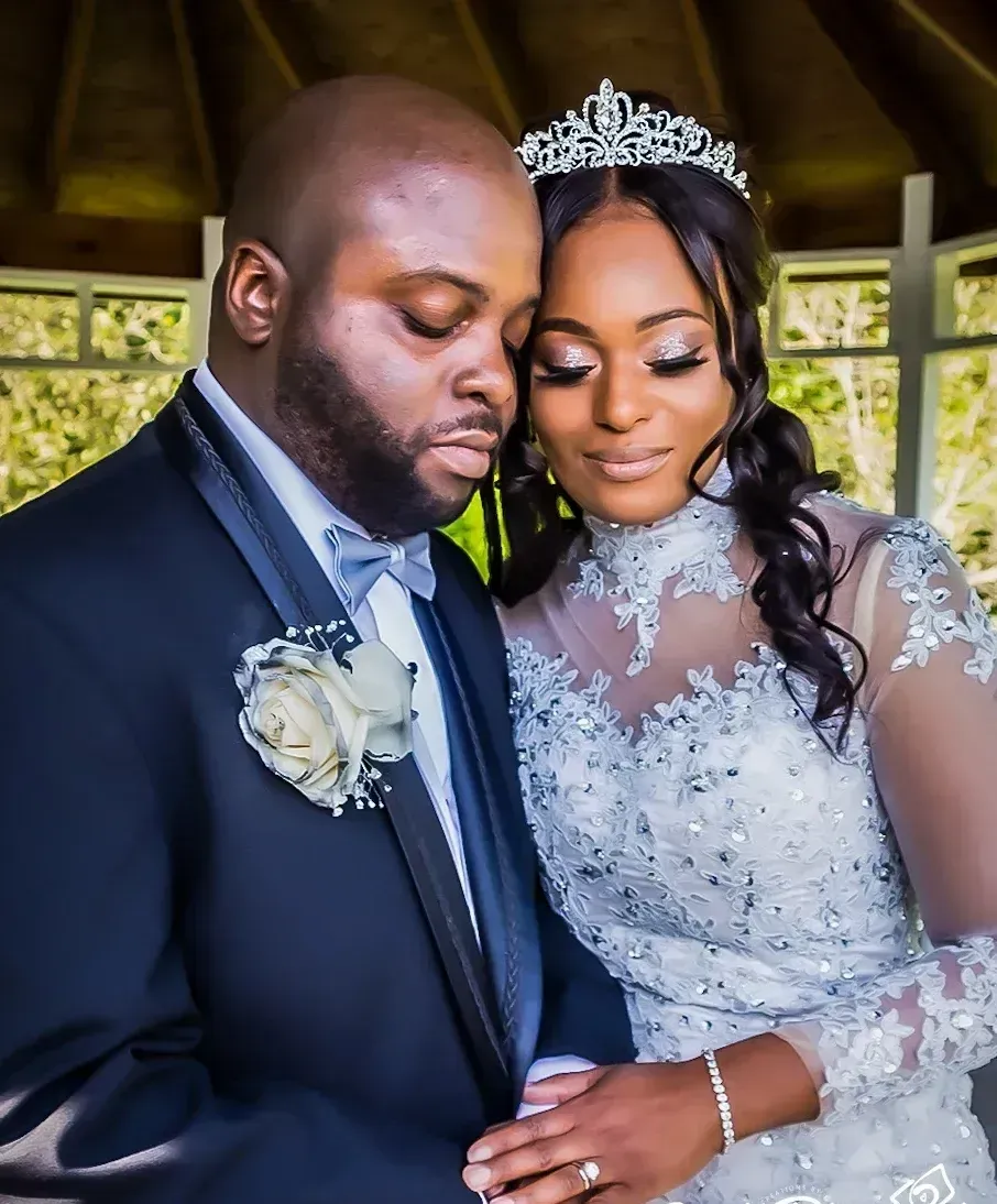 Bride and groom embracing, she wearing tiara and gown; he, dark suit with flower. Gazebo setting.