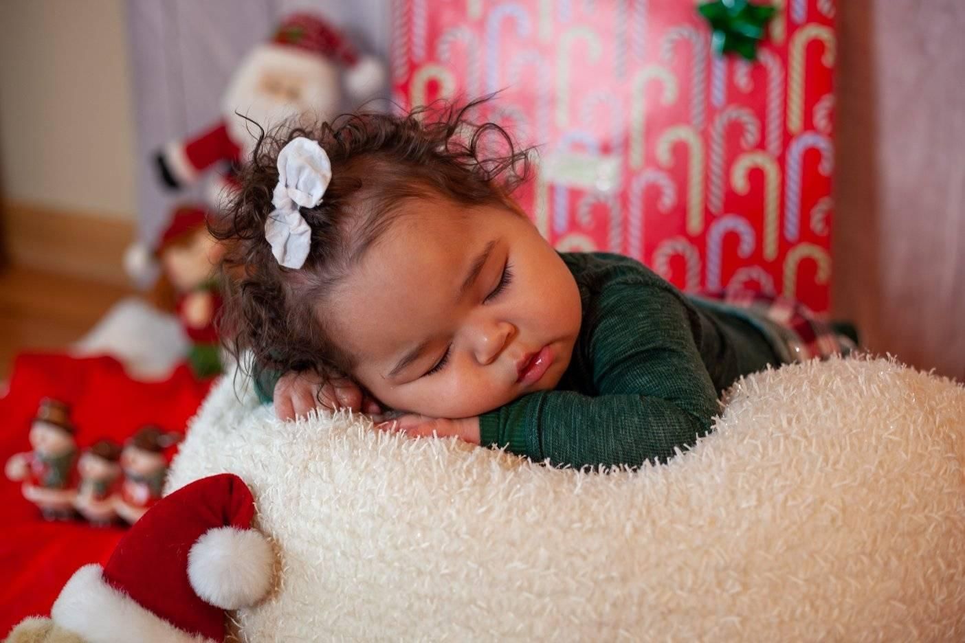 Baby sleeping on a soft, fluffy cloud prop, with Christmas decorations in background.