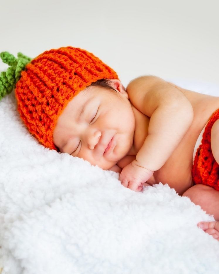 Newborn baby sleeping while wearing an orange knit hat