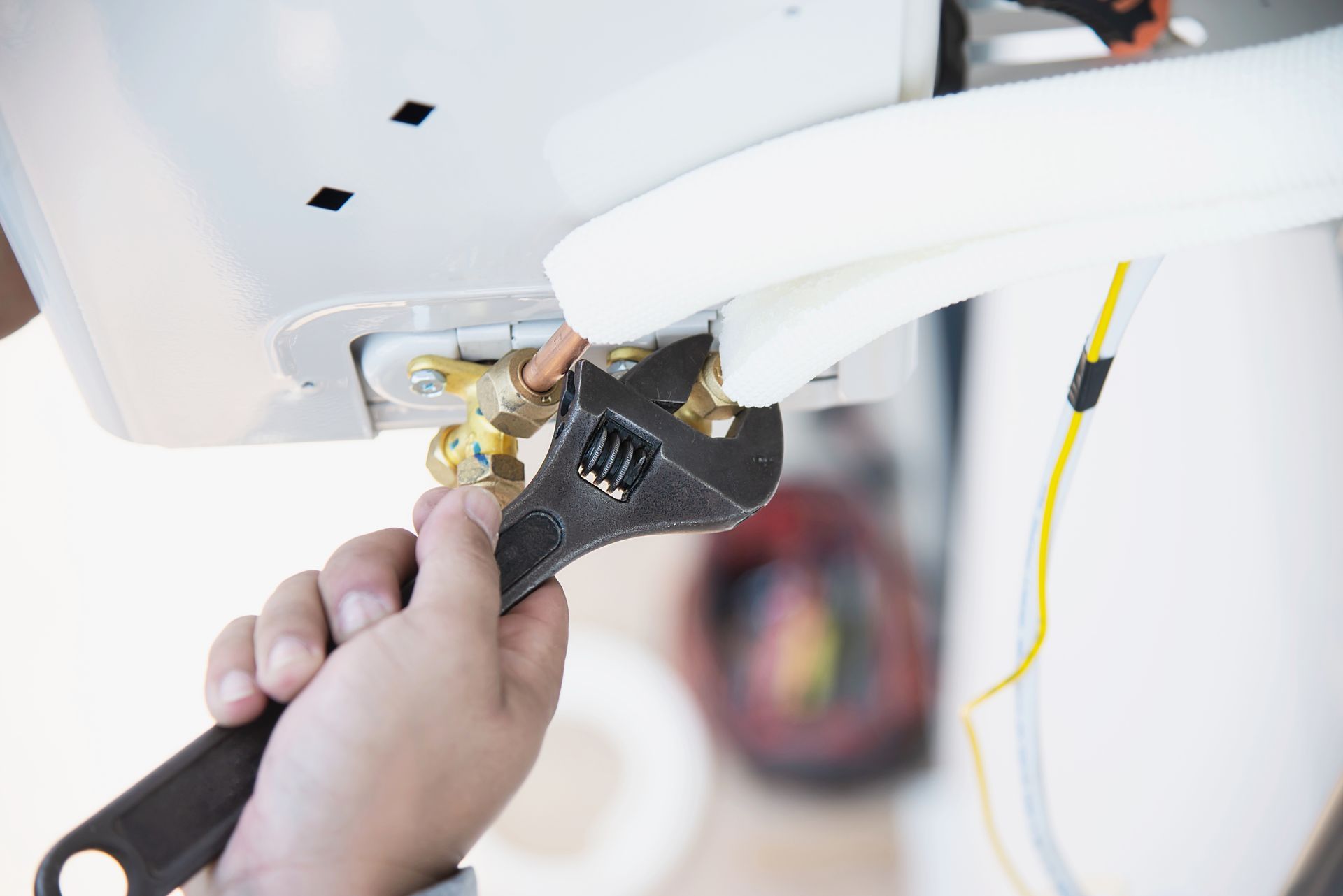 Hand using a wrench to tighten a brass fitting on a white appliance.
