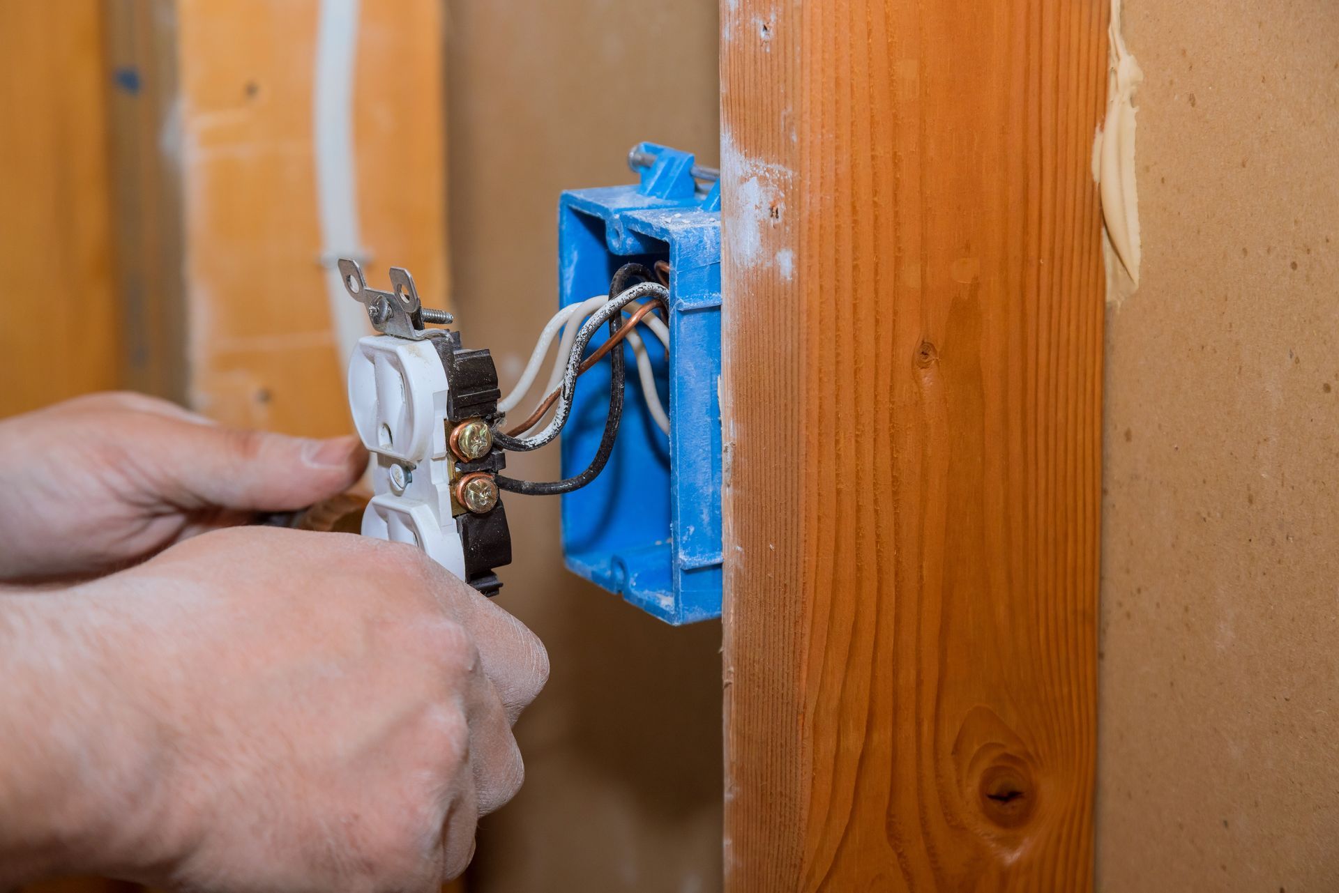 Hands wiring an electrical outlet into a blue box attached to a wooden beam.