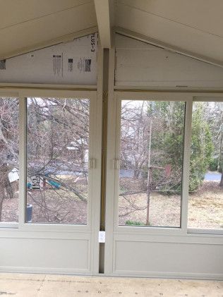 Two cream-colored windows side-by-side with a central support beam; view of trees and yard through the glass.