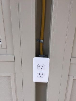 White electrical outlet with yellow cord in a recessed vertical channel, on a beige wall.