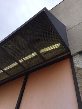 Black metal awning with a perforated design over a pink wall.