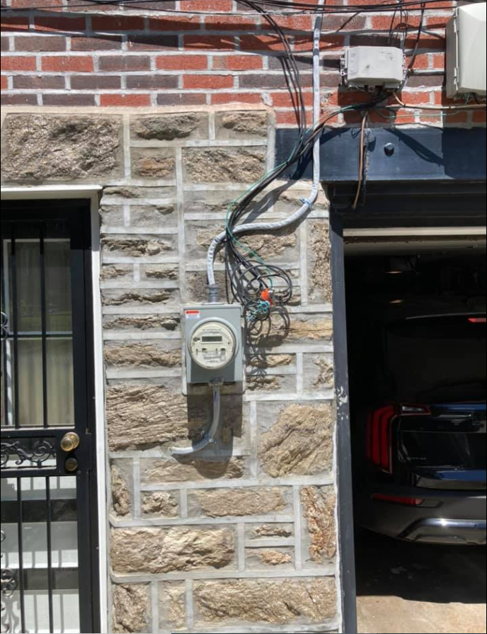 Exterior of building: electric meter and wiring on brick and stone facade next to a garage door.