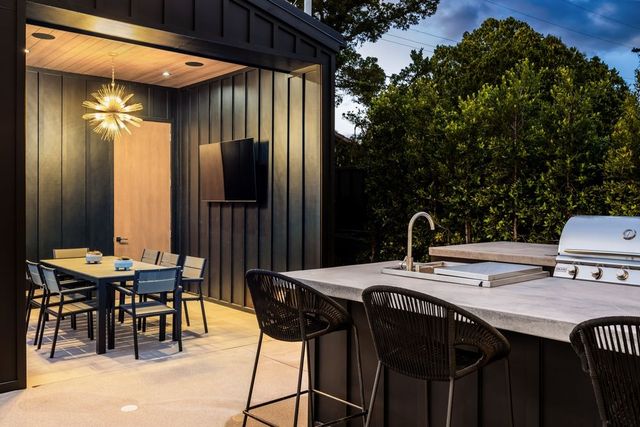 Outdoor kitchen and dining area with a bar, grill, and seating under a structure.