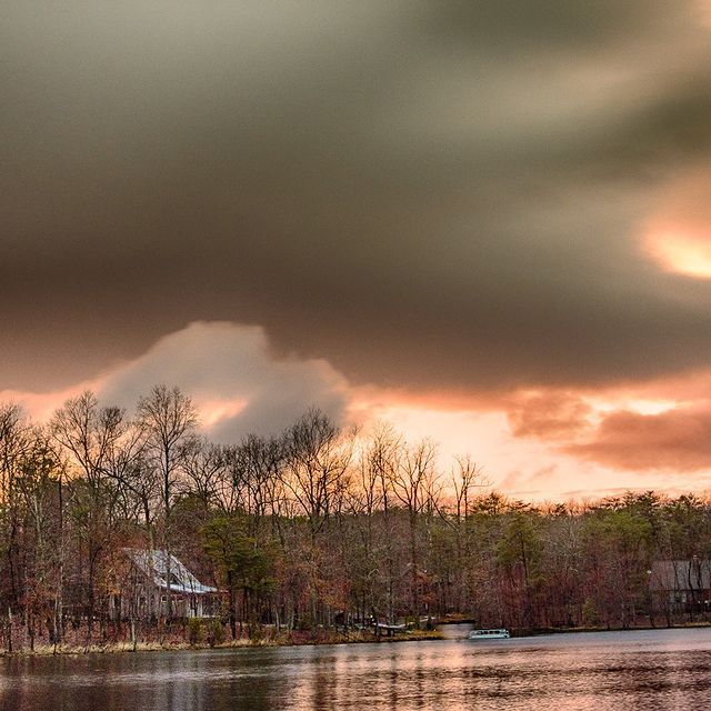 A lake surrounded by trees and a cloudy sky at sunset.
