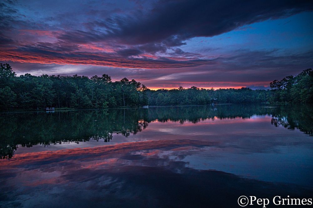 A lake with a sunset in the background and trees in the foreground.