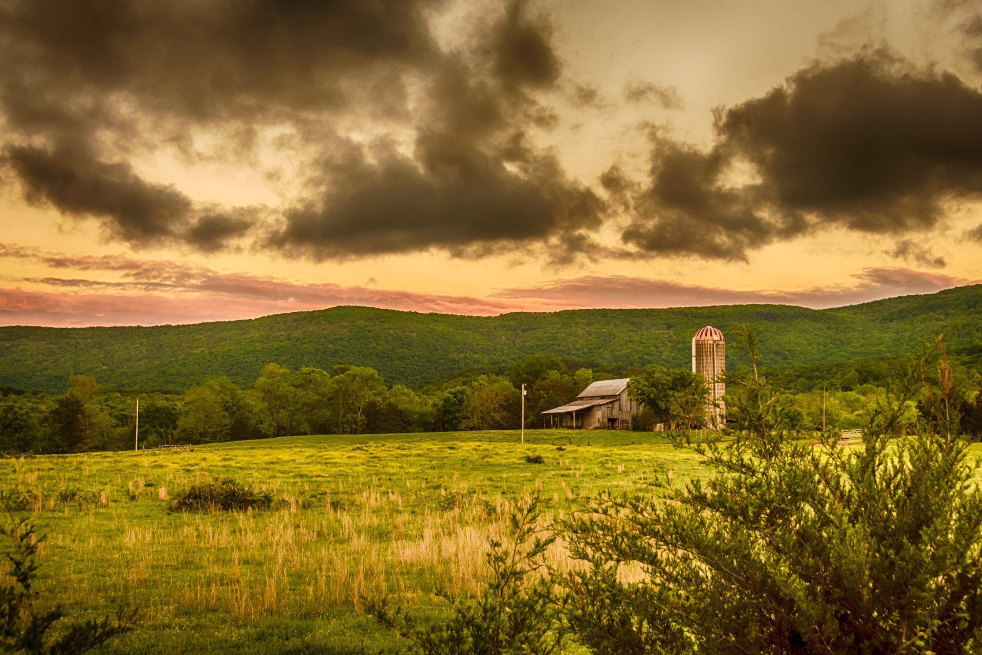 A barn and silo in a field with a cloudy sky in the background.
