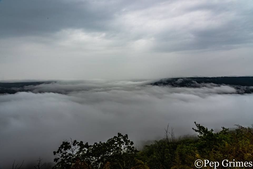 A view of a valley covered in clouds from a cliff.