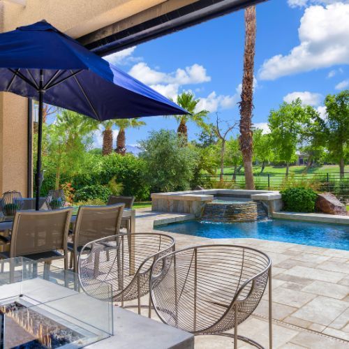 A patio with chairs and an umbrella overlooking a pool