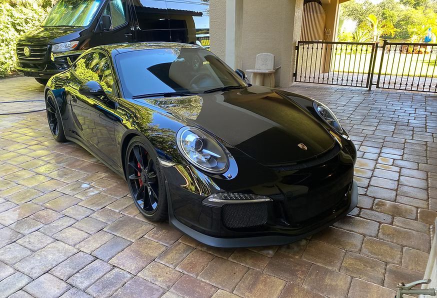 Black Porsche sports car parked on brick pavers.