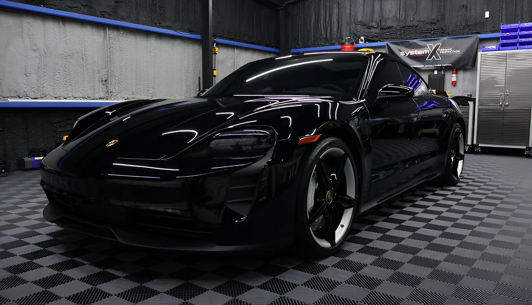 Black Porsche Taycan electric car parked on a checkered floor inside a garage.