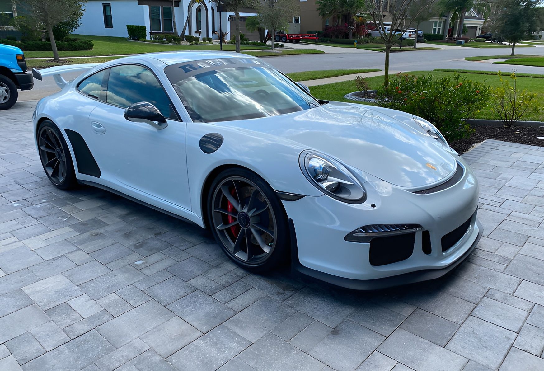 White Porsche 911 GT3 parked on a paved driveway in front of a house.