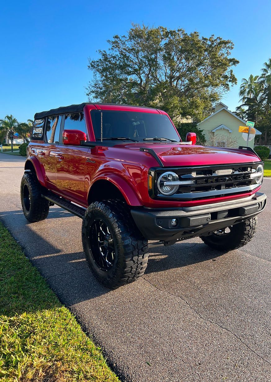 Red Ford Bronco SUV with black wheels, parked on asphalt with a blue sky background.