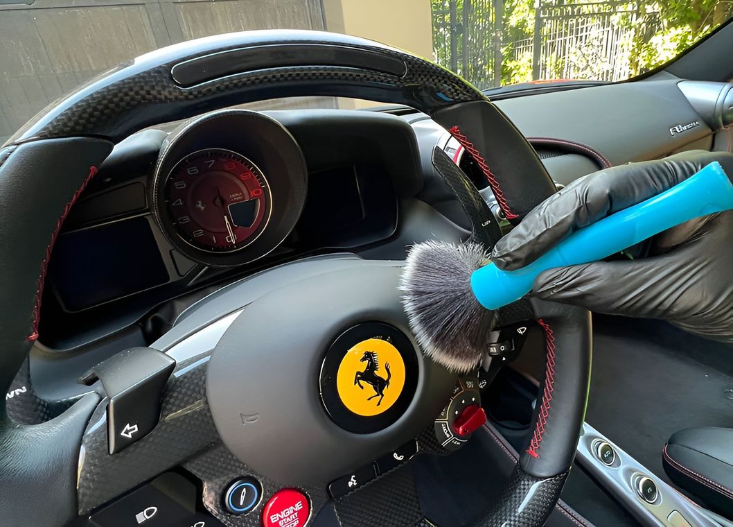 A person wearing black gloves cleans a Ferrari steering wheel with a blue brush.