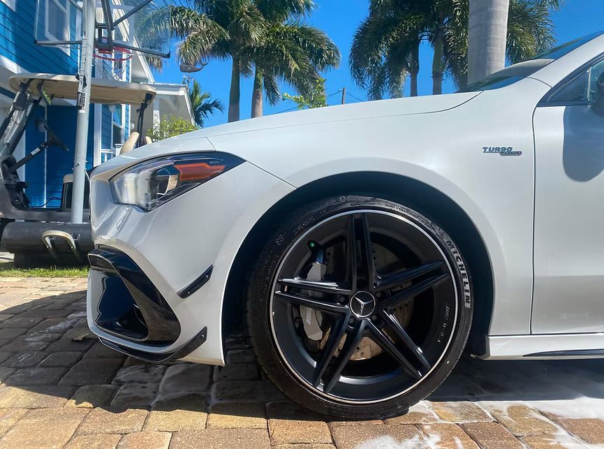 White Mercedes-Benz AMG car with black rims parked outside on a sunny day.