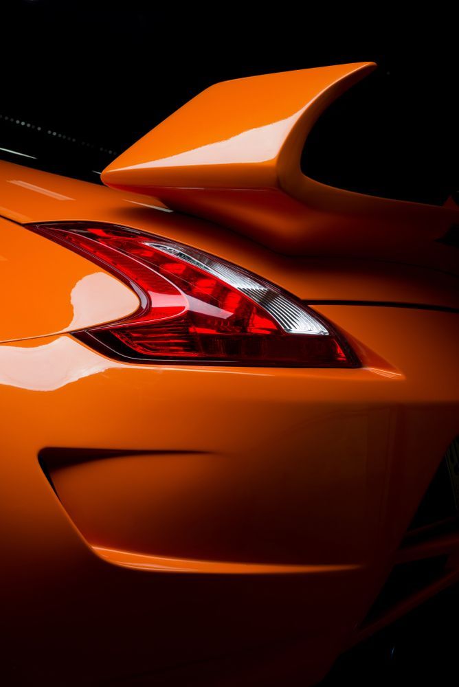 Orange sports car rear detail with spoiler and taillight, dark background.