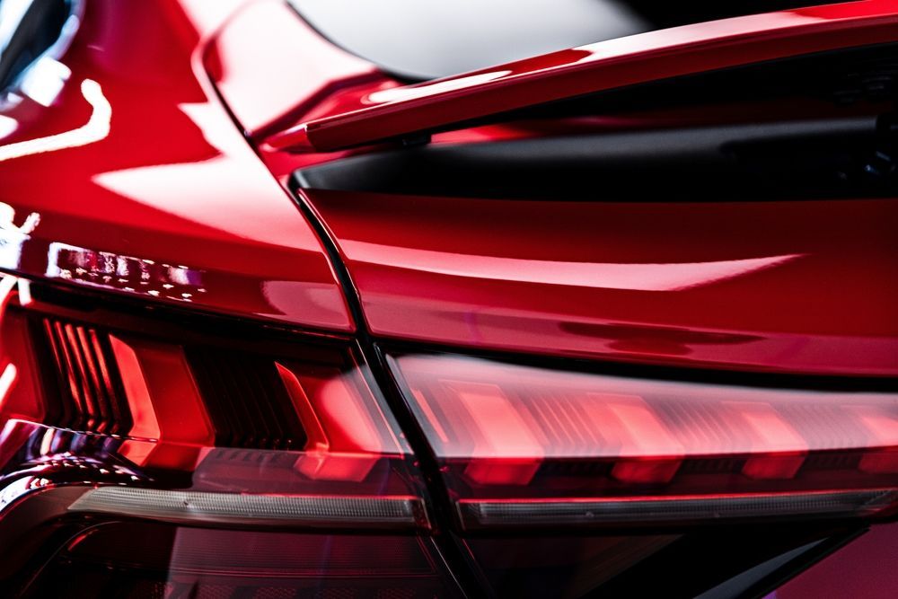 Red car's rear, showcasing its glossy paint, tail light, and spoiler.