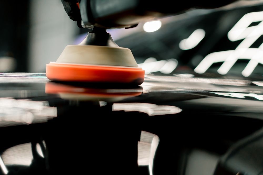 Polishing tool buffing a black car surface, reflecting bright light.