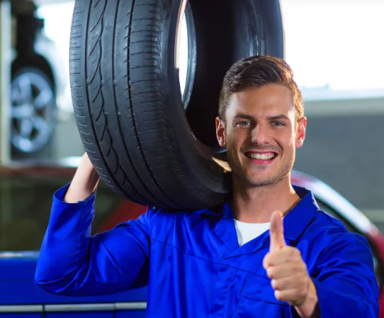 Um homem está segurando um pneu encima de seu ombro em uma garagem.