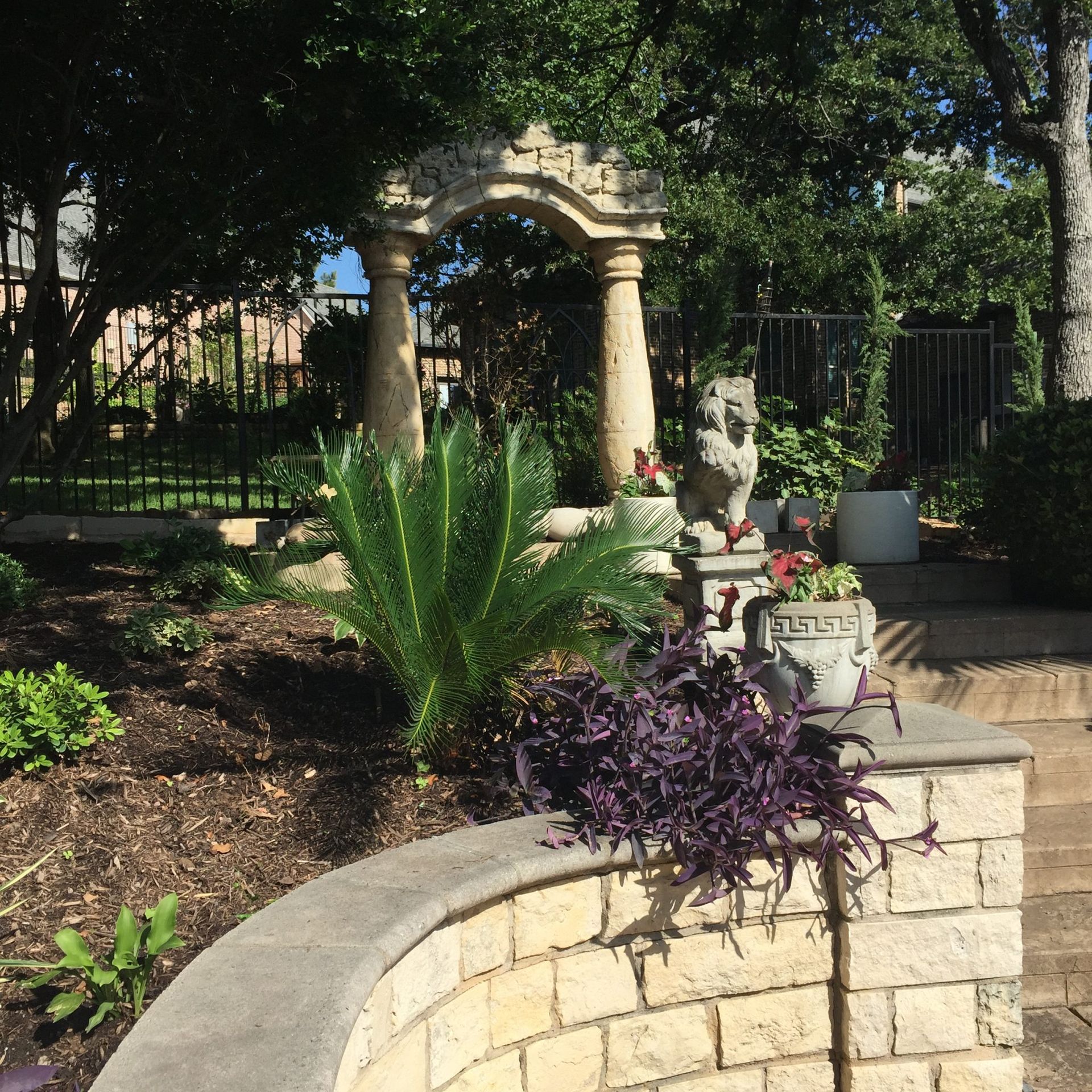 Stone archway and garden with purple foliage and small owl statue.