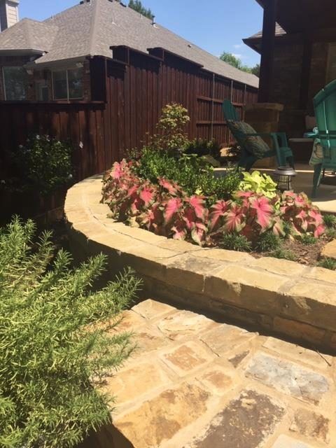 Stone patio with a curved retaining wall garden bed, brown fence, and house in the background.