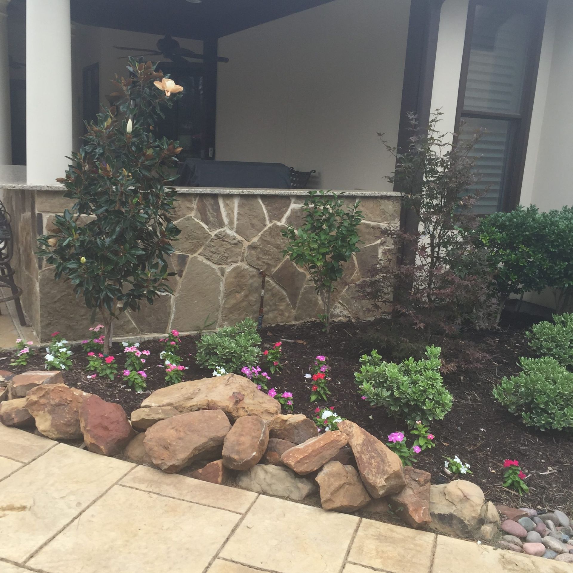 Landscaped yard with stone wall and a variety of plants and flowers.