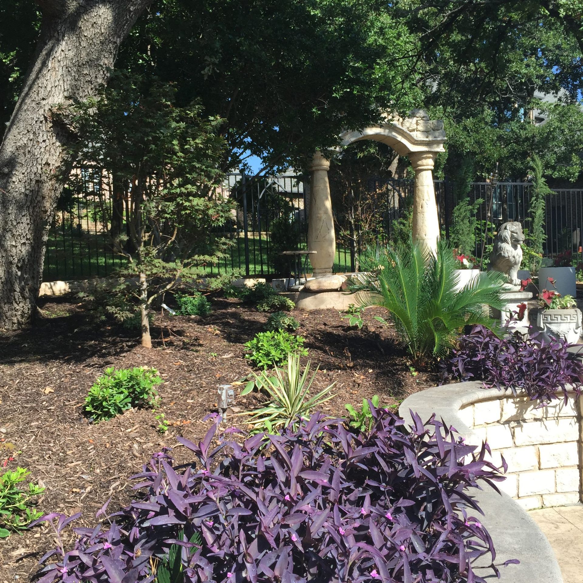 Landscaped garden with purple plants, stone archway, and mature trees.