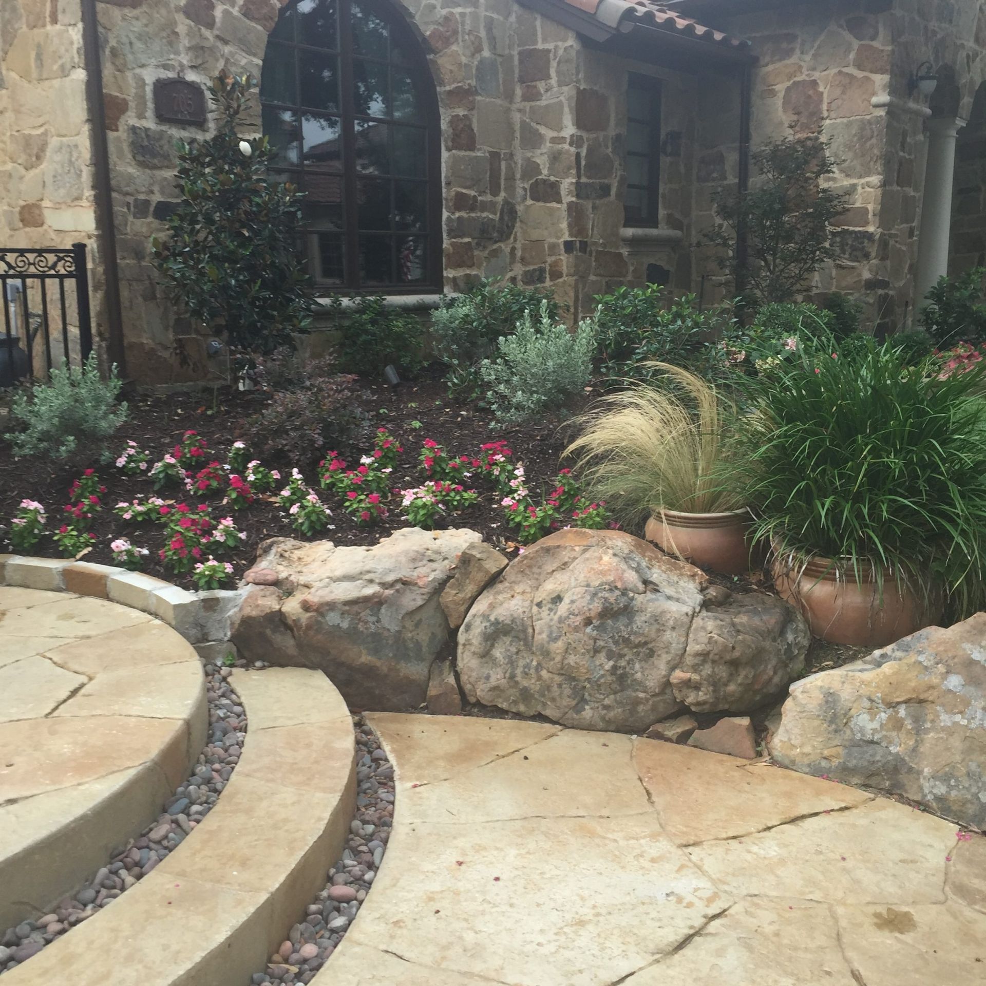 Stone pathway and garden with colorful flowers, large rocks, and a stone facade.