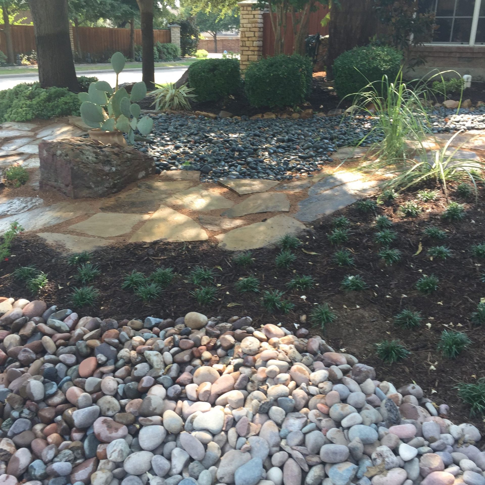 Landscaped yard with stone pathway, river rock, and various plants.