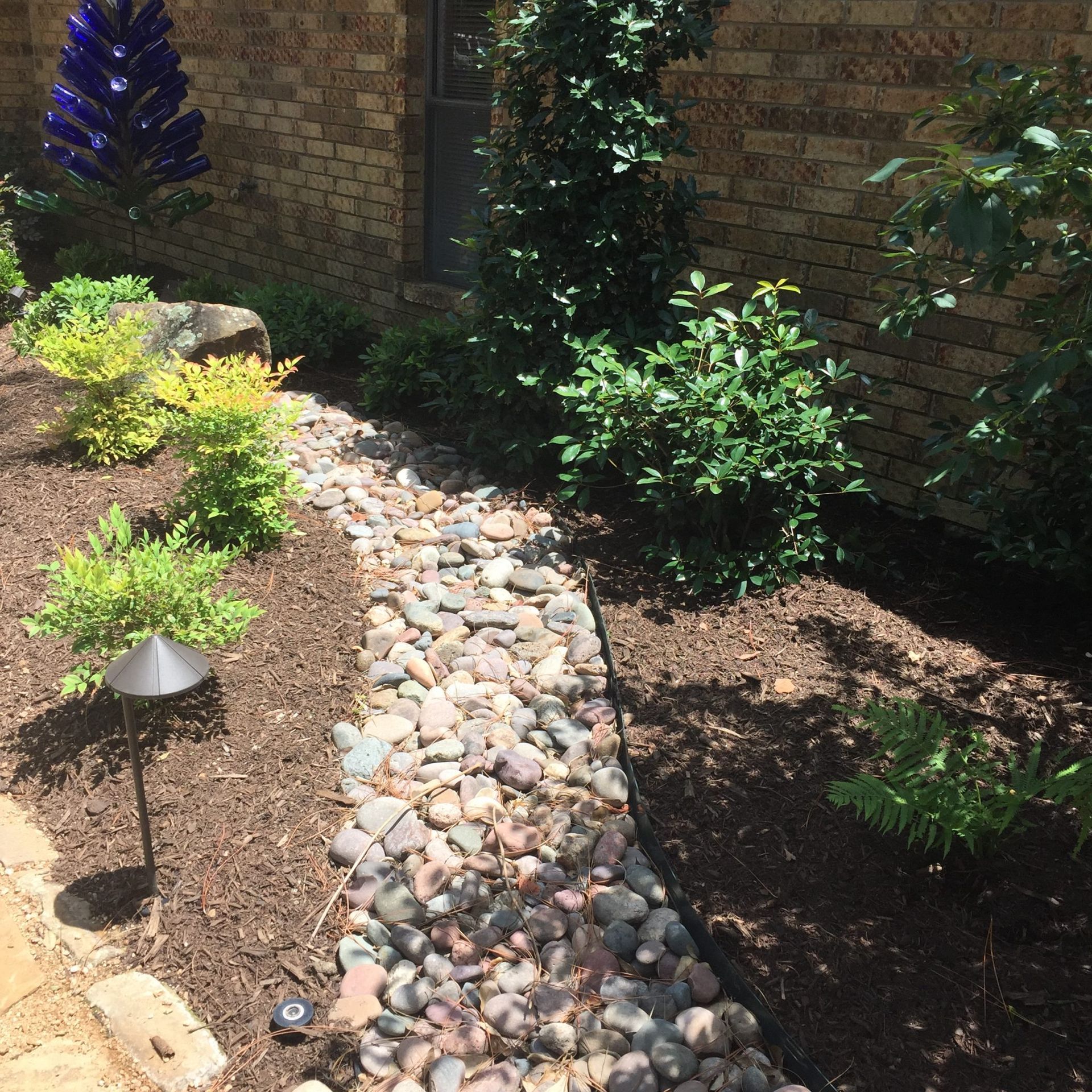 Dry creek bed with river rocks and landscaping, alongside a brick wall.