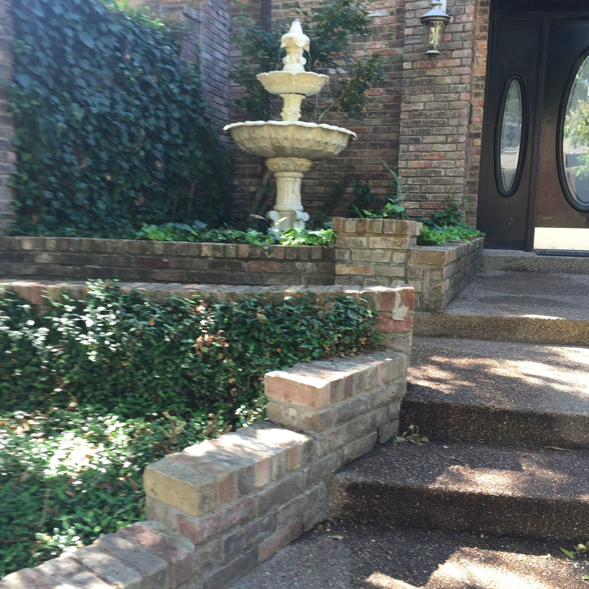Brick steps lead to a house with a fountain surrounded by greenery.