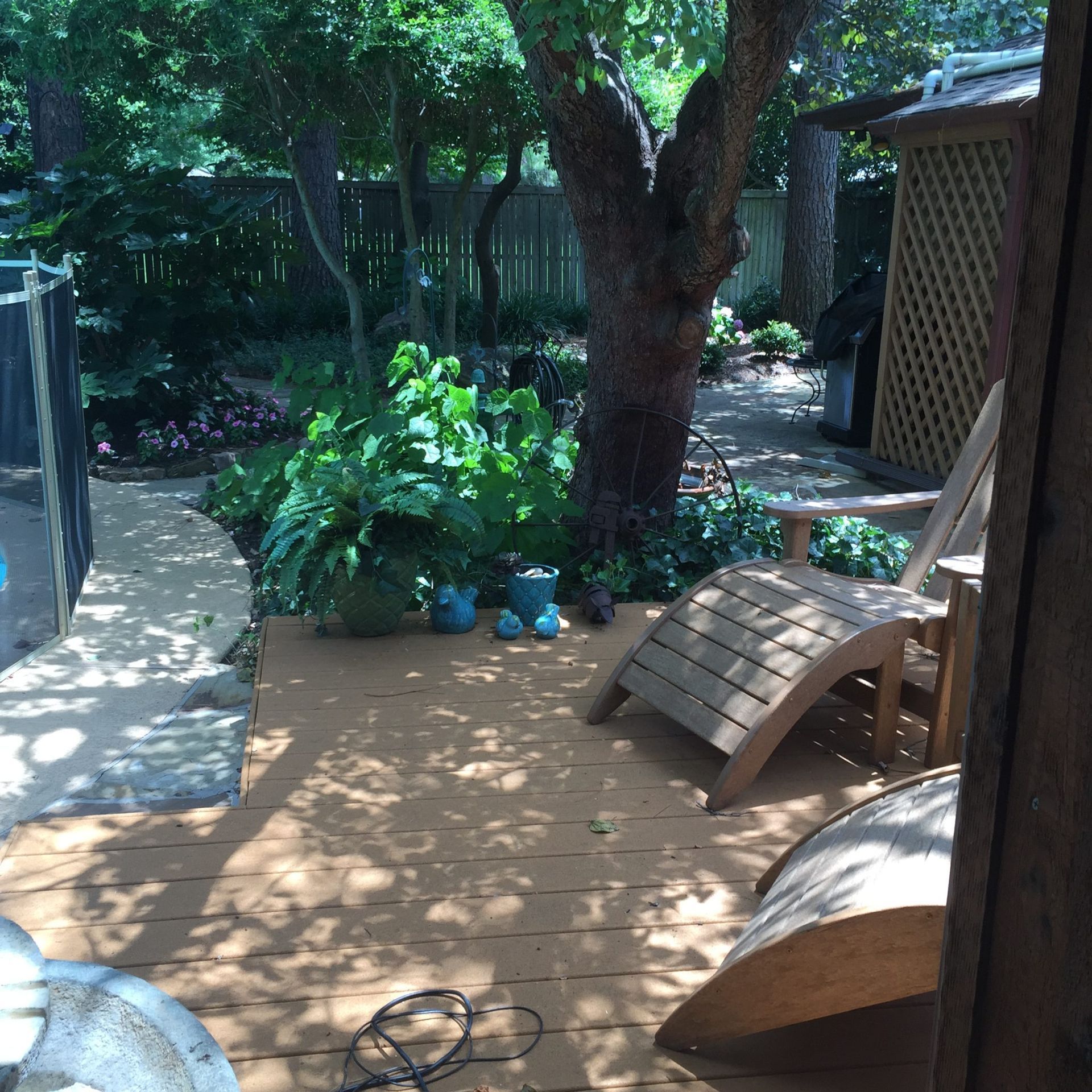 Wooden deck with chairs, large tree, and garden area.
