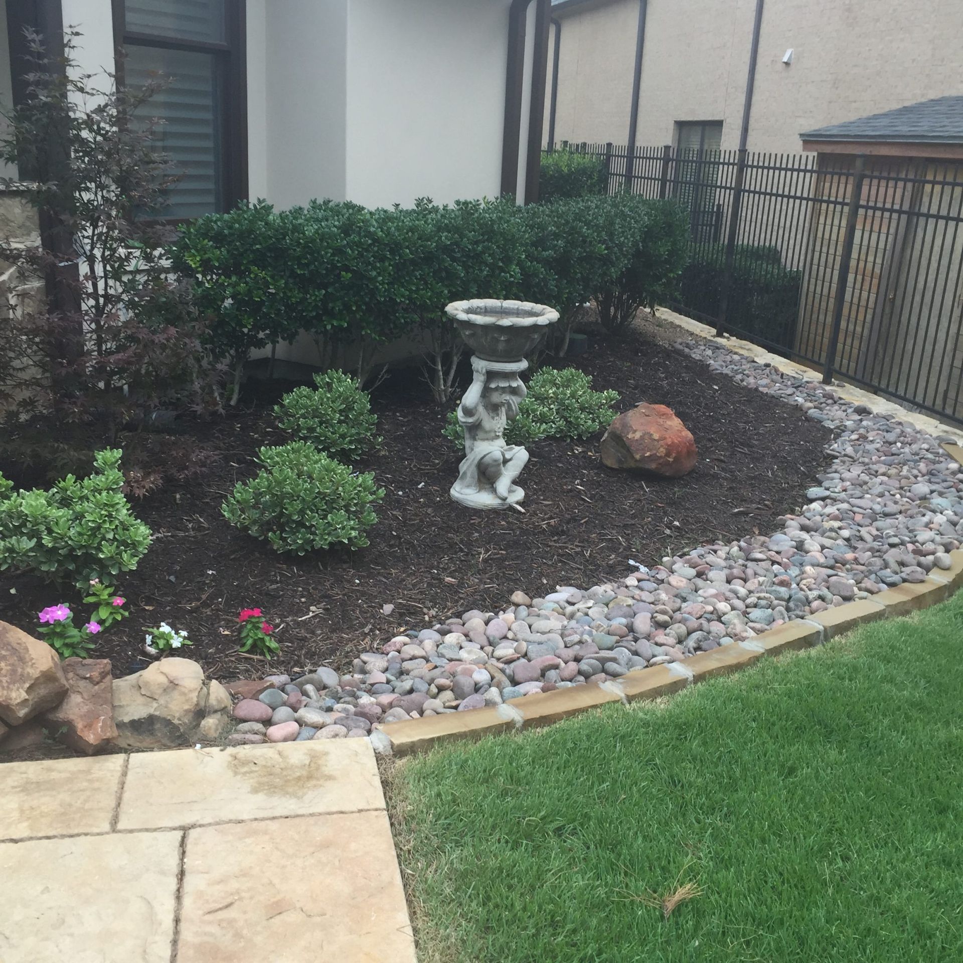 Landscaped garden bed with shrubs, statue, and stone border.