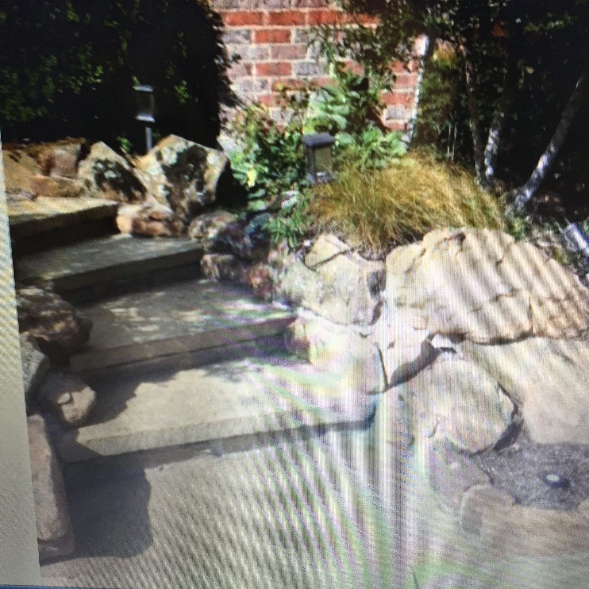 Stone steps lead up to a brick wall, flanked by large rocks and greenery.