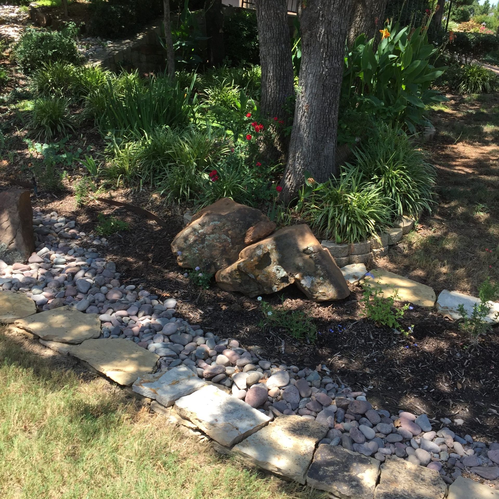 A landscaped garden bed with rocks, mulch, a tree, and plants with a stone border.