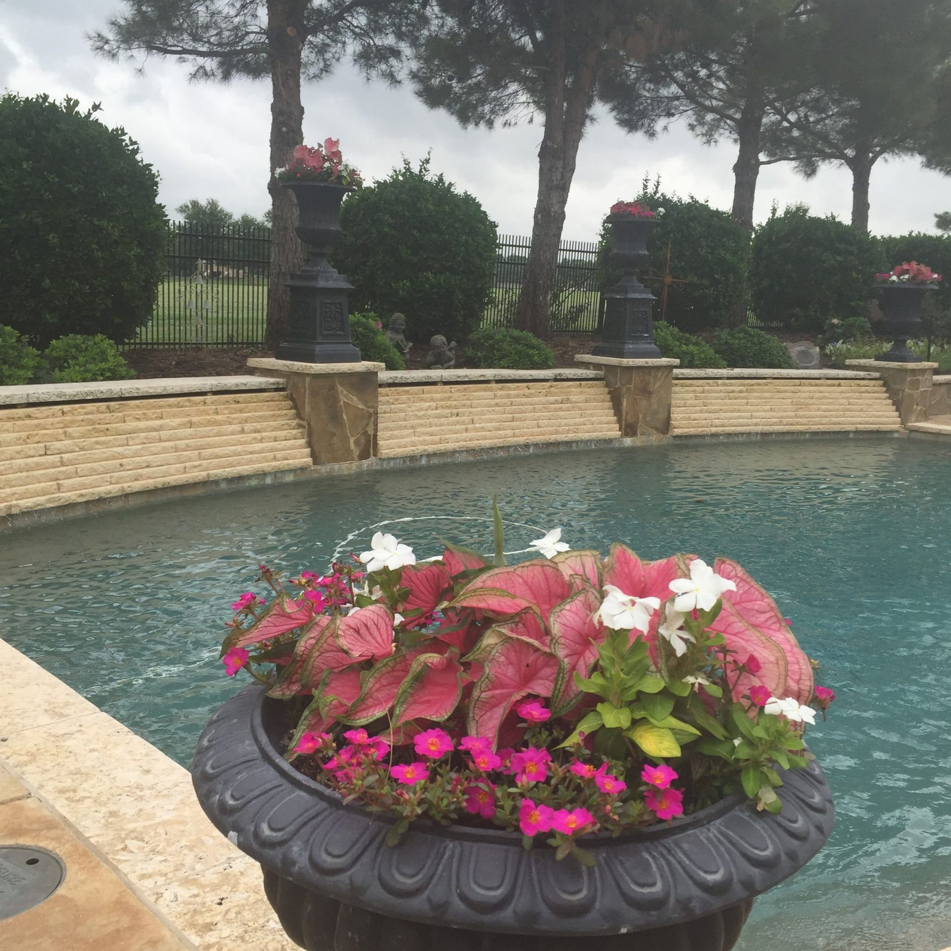 Poolside planter with red and white flowers, with water feature and stone structure.