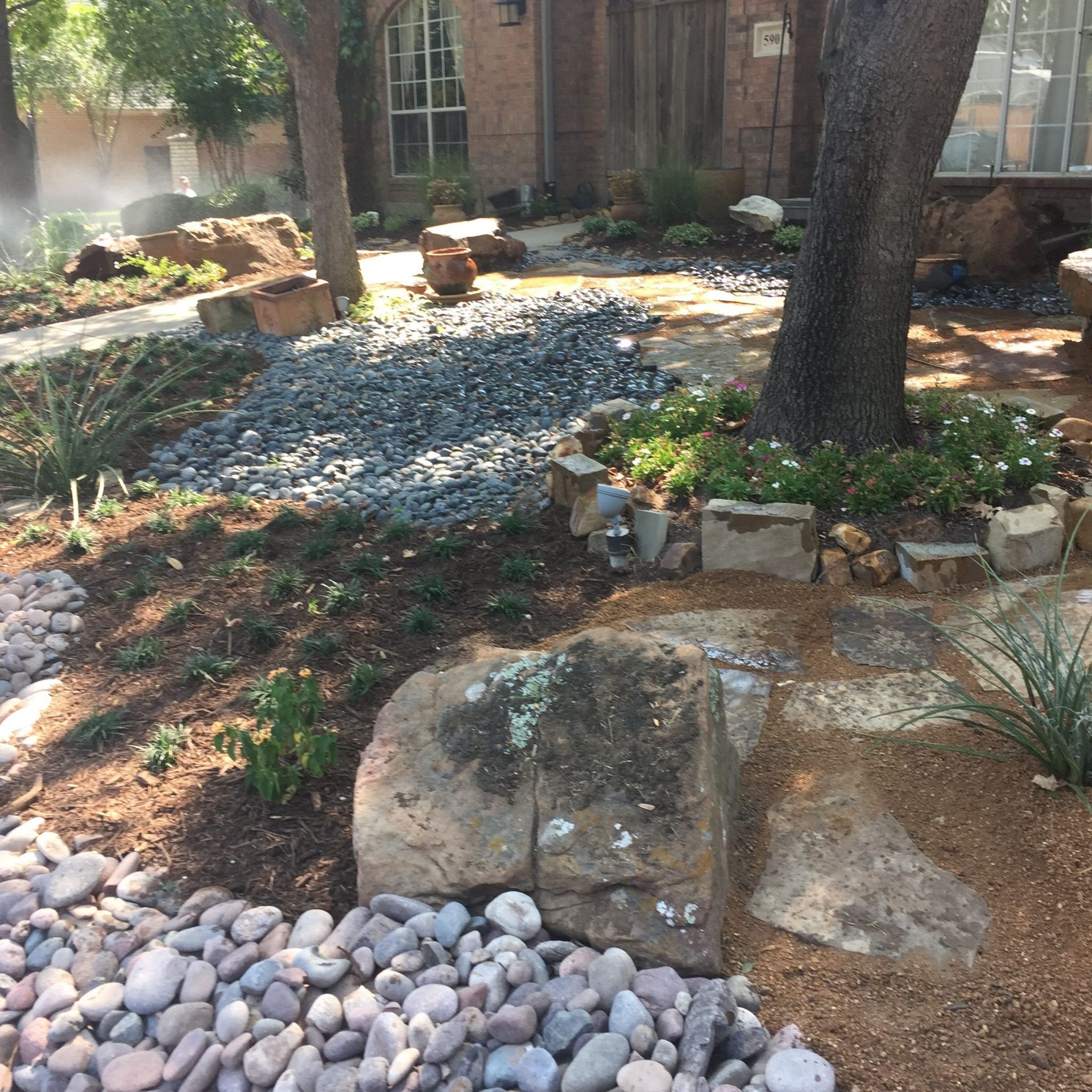Landscaped front yard with stone, gravel, plants, and trees.